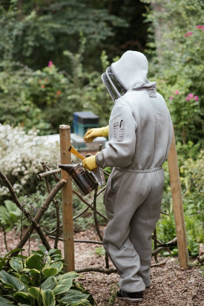 Beekeeper in full suit using a smoker in a lush, green apiary setting, highlighting sustainable farming.